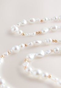 White irregular pearls and small gold beads strung together in a delicate necklace on a light surface.