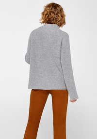 Pull en tricot côtelé gris avec col montant et manches longues, doté d'une coupe décontractée et de coutures raglan aux épaules, associé à un pantalon marron.