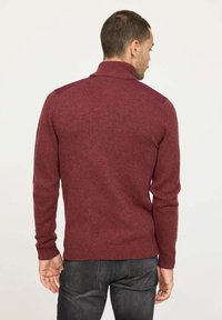 Pull en tricot bordeaux avec un col montant, design ajusté et accents sombres aux épaules. Texture douce avec des poignets et un ourlet côtelés.