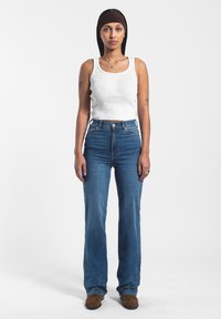 Top blanco de tirantes acanalado, jeans de mezclilla azul de cintura alta y botas marrones hasta el tobillo. Tela suave, parte superior ajustada, diseño de pierna acampanada en los jeans.