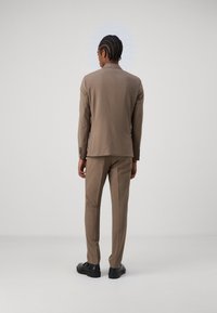 Completo marrone su misura con giacca a un petto e pantaloni slim-fit, abbinato a scarpe nere. Tessuto liscio e design classico.