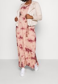 Maxime-mekko persikansävyssä, jossa on burgundin värinen tie-dye, yhdistettynä vaaleanbeigeen mokkanahkamoottorijackettiin ja valkoisiin lenkkitossuihin. Sujuva tekstuuri.