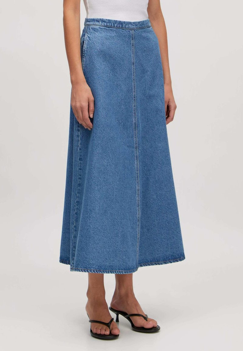 Jeans maxi rok in medium blauw, met een hoge taille, zijsplitten en een rechte silhoët met een schone zoom. Gestyled met zwarte sandalen.