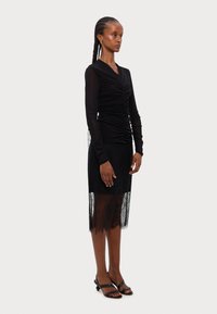 Black long-sleeve dress with gathered front detail; lace skirt hem; paired with black strappy sandals. Smooth and textured fabrics.