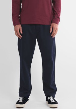 Pantalon bleu marine à jambes droites en tissu léger. Comprend des poches avant et est associé à des baskets noires et une chemise à manches longues bordeaux.