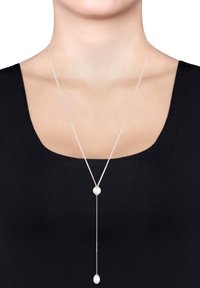 Zilveren hanger ketting met een Y-vormig ontwerp, met twee witte parels aan een dunne ketting. De achtergrond is zwart.