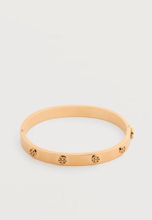 Armbånd i guldfarvet metal med fire små, runde dekorative nitter jævnt fordelt rundt om båndet.