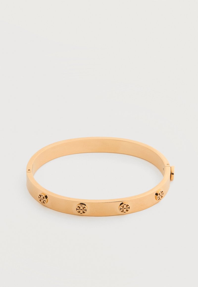 Βραχιόλι βέργας από μέταλλο με χρυσό τόνο, με τέσσερις μικρές στρογγυλές διακοσμητικές καρφίτσες τοποθετημένες ομοιόμορφα γύρω από τη ζώνη.