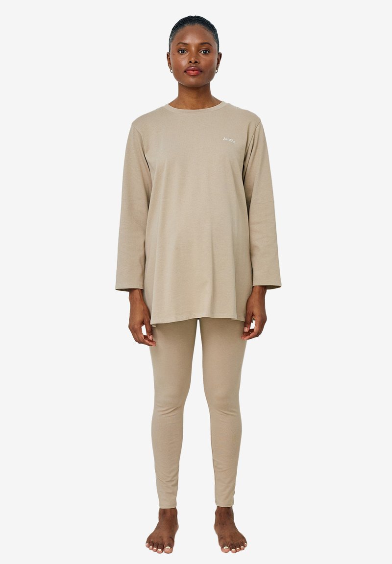 Beige Baumwolloberteil mit langen Ärmeln, kombiniert mit passenden Leggings. Es hat einen lässigen Schnitt und ein einfaches Design mit einem kleinen Logo auf der Brust.