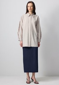 Light beige linen shirt with a collar and button details, paired with a navy long skirt and black strappy heels.