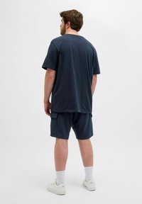 Marineblå bomulds T-shirt med korte ærmer, parret med matchende shorts med cargolommer, båret med hvide sneakers og ankelstrømper.