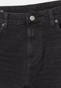 Vue de face de la taille d'un jean en denim noir avec bouton en métal, passants de ceinture et détails de couture visibles.
