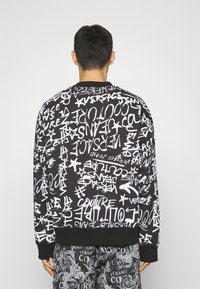 Černá mikina se bílým textem ve stylu graffiti a motivy hvězd; žebrované manžety a lem; zobrazeno zezadu.