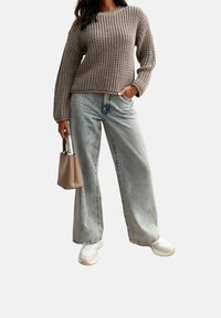 Gruby beżowy sweter, jasnoniebieskie szerokie dżinsy i białe sneakersy. Nosi małą beżową torebkę. Miękka tekstura i casualowy styl.