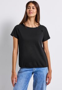 Zwarte top met korte mouwen en een ronde halslijn, gemaakt van glad fabric. Mesh accenten op de schouders. Rechte snit, casual pasvorm, gedragen met blauwe jeans.
