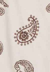 Witte stof met ingewikkelde bruine paisley borduursels, met bloemenmotieven en ronde accenten, die getuigen van gedetailleerd vakmanschap.