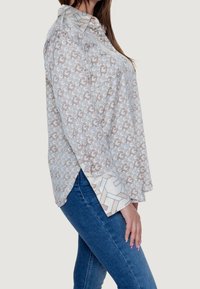 Blouse légère à manches longues avec un motif géométrique beige et blanc, dotée d'un col et de poignets à motifs contrastants.