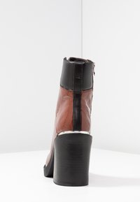 Bottine marron et noire avec une finition brillante, talon bloc haut, fermeture éclair latérale et panneaux texturés contrastants.