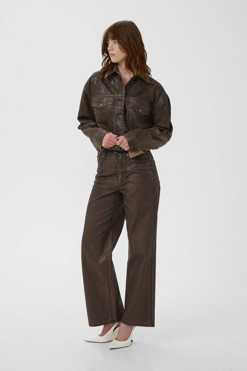 Dark brown denim jacket with chest pockets and matching wide-leg jeans. Smooth texture, casual design, paired with white pointed heels.