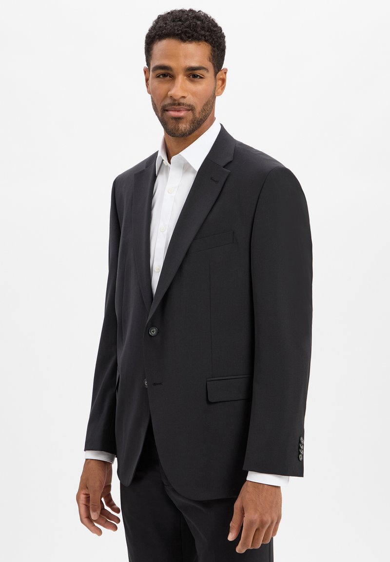 Blazer nero con un design strutturato, chiusura a un bottone e due tasche frontali. Accompagnato da una camicia bianca sotto.