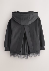 Veste noire à capuche avec panneau arrière plissé et bordure en dentelle le long de l’ourlet, présentée sur un fond uni clair.
