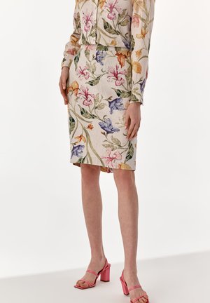 Jupe en lin à motif floral avec une silhouette ajustée, présentant des fleurs multicolores sur un fond beige clair. Talons roses à lanières assortis.