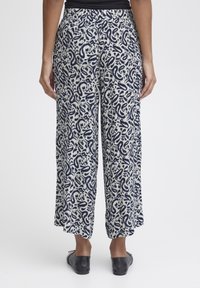 Un pantalon large en base crème avec un motif cachemire bleu marine, doté d'une taille élastique et d'une coupe décontractée, associé à des chaussures noires à enfiler.