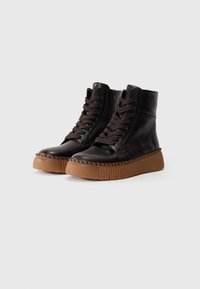 Bottines en cuir noir avec un laçage à l'avant et une fermeture éclair sur le côté. Semelle en caoutchouc brun épais et texturé avec un détail cousu autour du bord.