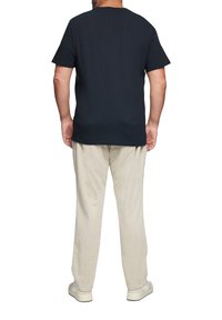 Marineblauw T-shirt met korte mouwen heeft een ronde hals, gecombineerd met lichtbeige corduroy broeken en witte sneakers, gezien vanuit de achterkant.