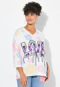 T-shirt w dekolcie w serek, w oversize'owym kroju, w kolorze białym z kolorowymi wzorami kwiatowymi. Posiada wyrazisty, kapiący napis "LOVE" w kolorach purpurowym i czarnym.