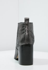 Schwarze Knöchelstiefel mit einer strukturierten, schlangenartigen Oberfläche, robustem Blockabsatz und einer hinteren Ziehlasche, die eine definierte und elegante Silhouette aufweisen.