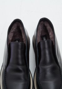 Chaussures en cuir noir à enfiler avec une doublure sombre et duveteuse, vues de dessus sur un fond clair.
