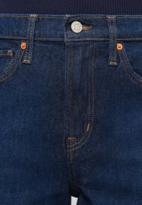 Tumesinised teksapüksid klassikalise viie tasku disainiga, kontrastse oranži õmblusega ning vöökohal hõbedase tooni metallist nööbiga.