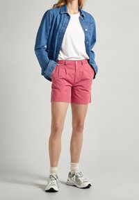 Giacca in denim, t-shirt bianca, pantaloni corti rosa brillante e scarpe sportive grigie. Il tessuto è morbido con una consistenza liscia e linee di design pulite.