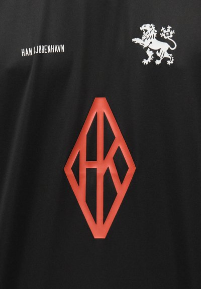 Black shirt featuring a white lion emblem and the text "HAN I JOBENHAVN." The front displays a prominent red diamond-shaped logo.