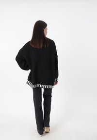 Zwart oversized gebreid sweater met witte gestreepte zoom, gecombineerd met zwarte broek. De sweater heeft een ontspannen pasvorm en verlaagde schoudernaden.