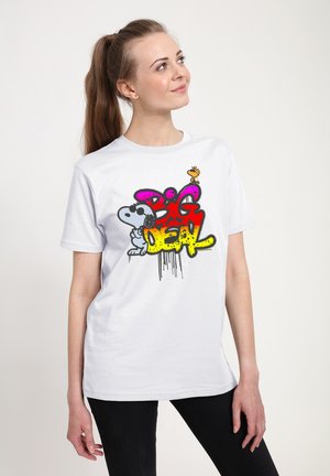 Ung kvinde med brunt hår i hestehale har en hvid T-shirt på med farverig graffiti tekst "Big Deal" og tegneserie Snoopy med Woodstock.