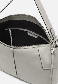 Jasnoszara skórzana torba o gładkiej fakturze, z główną komorą zapinaną na zamek oraz wewnętrzną kieszenią na zamek. W zestawie regulowany pasek.