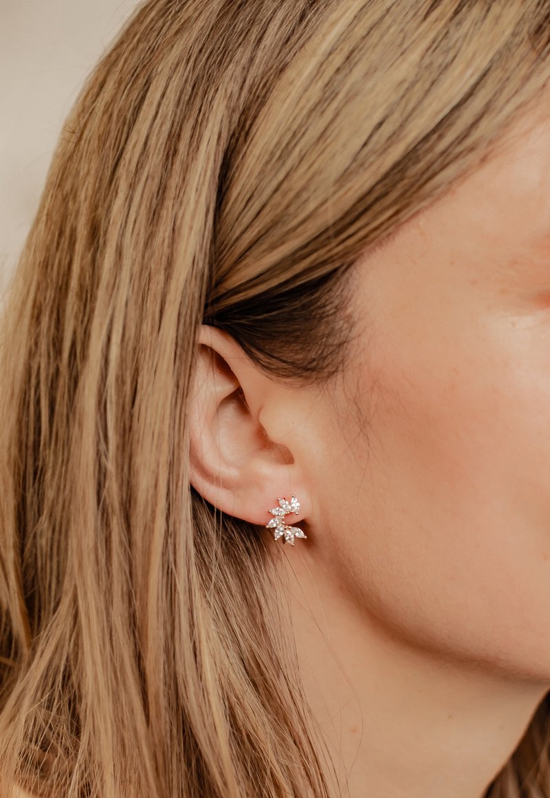 Ohrringe in Roségold mit floralem Design, die mit marcasit- und runden Zirkonia-Steinen verziert sind, vor einem sanft strukturierten Hintergrund.