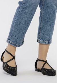Ballerine nere intrecciate con punta aperta, caratterizzate da un design testurizzato, fasce incrociate e un tacco basso. Indossate con jeans denim risvoltati.