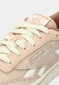 Sneaker Reebok Classic di colore rosa chiaro con lacci bianchi, strisce bianche ai lati e logo Reebok con la Union Jack sul pannello laterale.