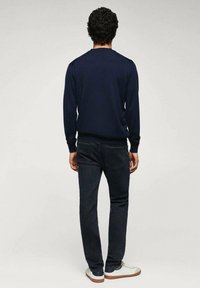 Pull marine à col rond avec poignets côtelés, associé à un jean foncé. La tenue est complétée par des baskets blanches au design simple et classique.