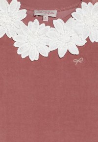 Růžové bavlněné tričko s bílým krajkovým límečkem zdobeným perlami. V dolním rohu je jemně vyšitá mašle.