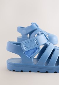 Sandales bleues pour enfants en plastique texturé, avec un design segmenté, une sangle ajustable et une semelle en caoutchouc antidérapante.