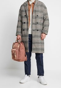 Harmaa ja valkoinen ruudullinen takki, ruskea corduroy-paita, kermanvärinen villapaita, tummat farkut, pidä pinkkiä reppua vaaleilla yksityiskohdilla, valkoiset lenkkarit.