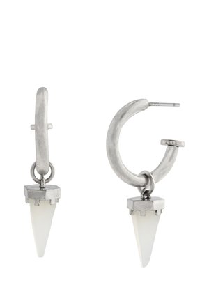 Boucles d'oreilles créoles en métal argenté avec pendentifs en pierre blanche triangulaire suspendus à chaque créole sur fond blanc.