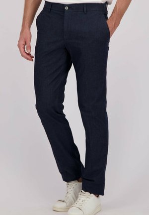 Marineblauwe tailor-made broek van een lichtgewicht stof, met rechte pijpen, voorzakken en een enkele knoopsluiting. Gecombineerd met witte sneakers.