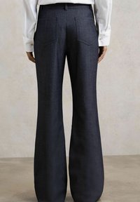 Pantaloni evazați de culoare albastru închis, dintr-un material neted și texturat. Prezintă două buzunare spate și un brâu croit, purtați împreună cu o cămașă albă.