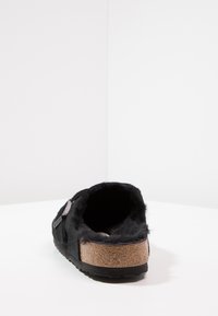 Pantofole nere con fodera in pelliccia, soletta in sughero e suola in gomma. Presentano una fascia laterale e una texture morbida, progettate per il comfort.