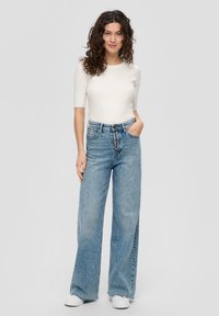 Witte aansluitende ribgebreide top gecombineerd met hoge lichte blauwe wijde jeans met knoopsluiting, zijzakken en een ontspannen pasvorm.